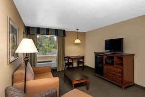 Une chambre d’hôtel avec un canapé, une petite table, un téléviseur posé sur un meuble en bois et une fenêtre avec des rideaux.