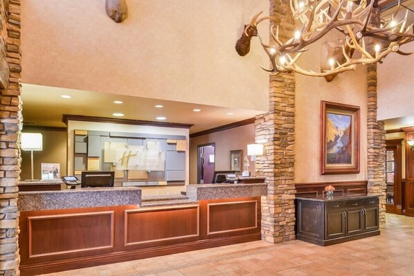 A reception area with a stone pillar, a chandelier, and a framed painting on the wall. - The Evergreen Hotel (McCall)