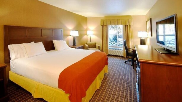 Una habitación de hotel con una cama grande, lámparas de noche, un escritorio con televisor y una ventana con cortinas.
