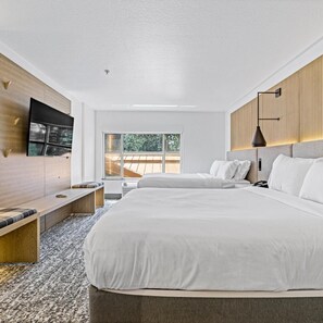 Une chambre d’hôtel moderne avec un grand lit, un téléviseur fixé au mur, un banc et une fenêtre donnant sur l’extérieur.