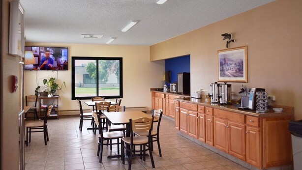 A dining area with tables and chairs, a kitchen counter with appliances, and a television on the wall. - Surestay by Best Western Glendive Yellowstone River (Glendive)