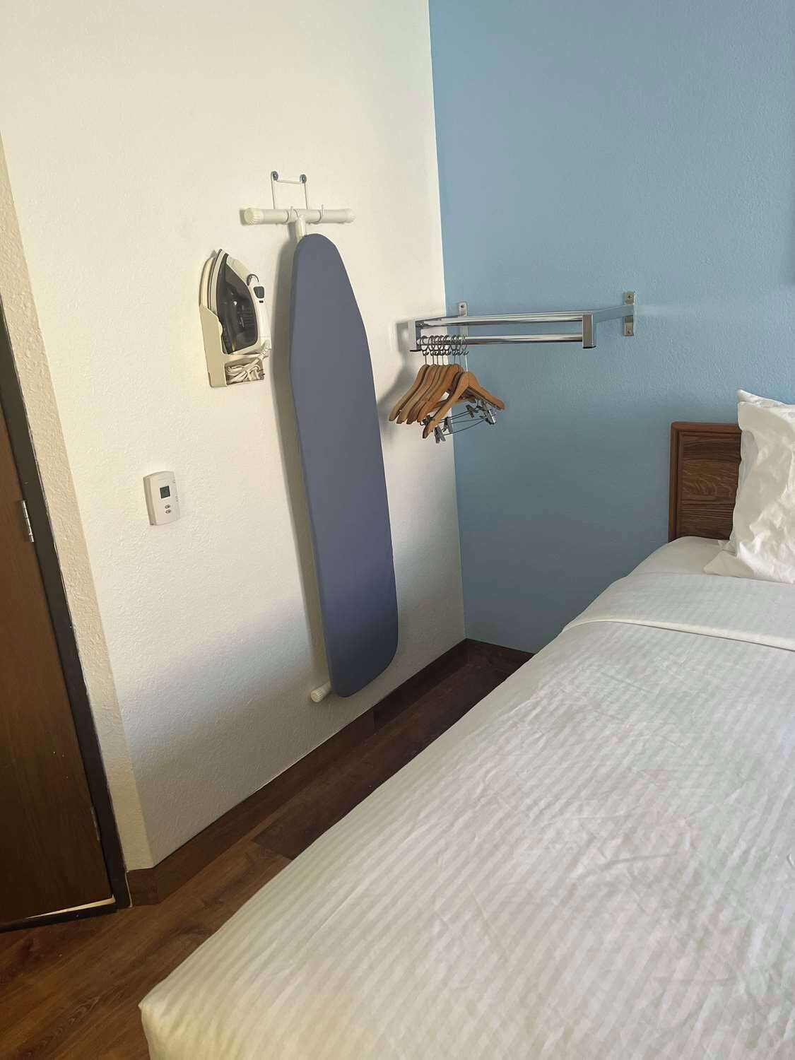 Une chambre d’hôtel équipée d’un lit, d’une planche à repasser fixée au mur, d’un étendoir et d’un thermostat.