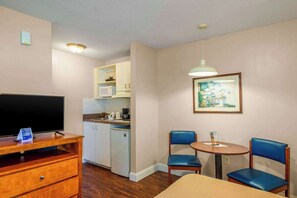Habitación de hotel compacta con televisión, una kitchenette pequeña, comedor para dos personas y un cuadro en la pared.