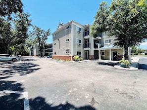 A multi-story building with a parking lot, trees, and a clear sky. - Suburban Studios Airport (Tampa)