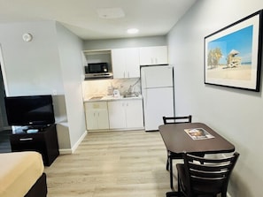 A compact living space with a kitchenette, a dining area with a table and chairs, a flat-screen TV, and a framed picture on the wall. - Suburban Studios Airport (Tampa)