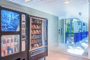 Máquina expendedora con diferentes snacks y bebidas, un botón pulsador y un dispensador de Coca-Cola.