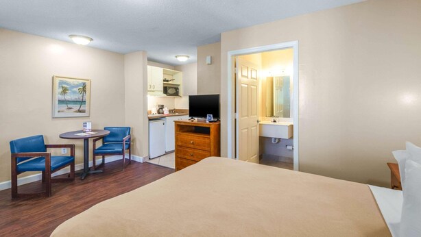Une chambre d’hôtel comprenant un lit, un bureau avec une chaise, une télévision, une petite kitchenette et une salle de bain.