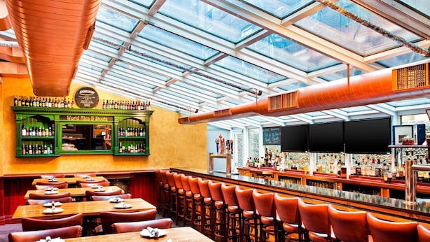 Een bar met glazen dak, houten tafels en een groene barwinkel met de tekst 'World Wines & Stouts'.