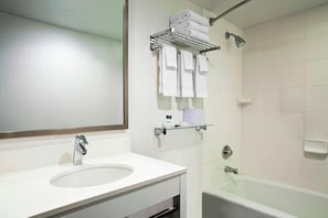 Un baño con un lavamanos blanco, un espejo, repisas de vidrio con toallas y una bañera.