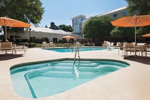 Une piscine entourée de chaises longues et de parasols, le tout bordé par un bâtiment sur lequel est apposée une enseigne.