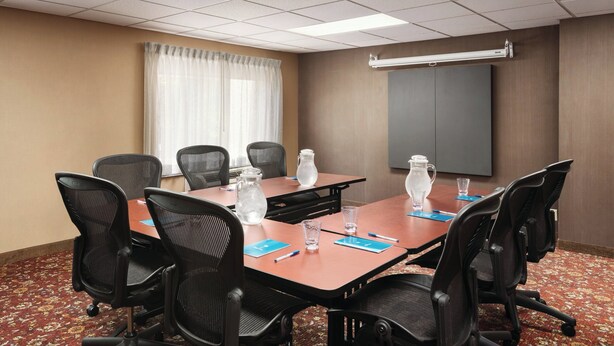 A conference room with a long table, black chairs, water pitchers, and a projector screen. - CLT Sky Suites (Charlotte)