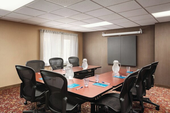 A conference room with a long table, black chairs, water pitchers, and a projector screen. - CLT Sky Suites (Charlotte)