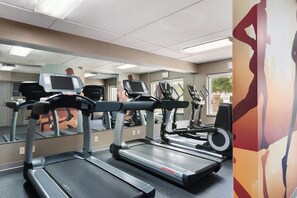 Un gimnasio con cintas de correr, bicicletas estáticas y espejos.