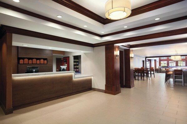 A reception area with a wooden reception desk, a counter, and a seating area with tables and chairs. - CLT Sky Suites (Charlotte)