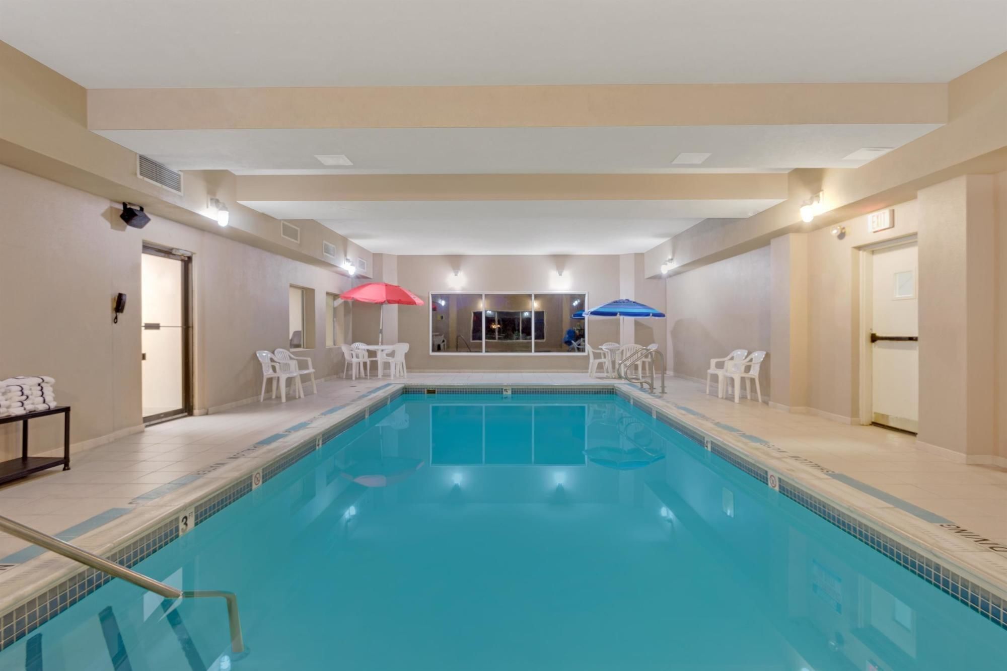 An indoor swimming pool with clear lane markings, two umbrellas, and white chairs around the pool area.