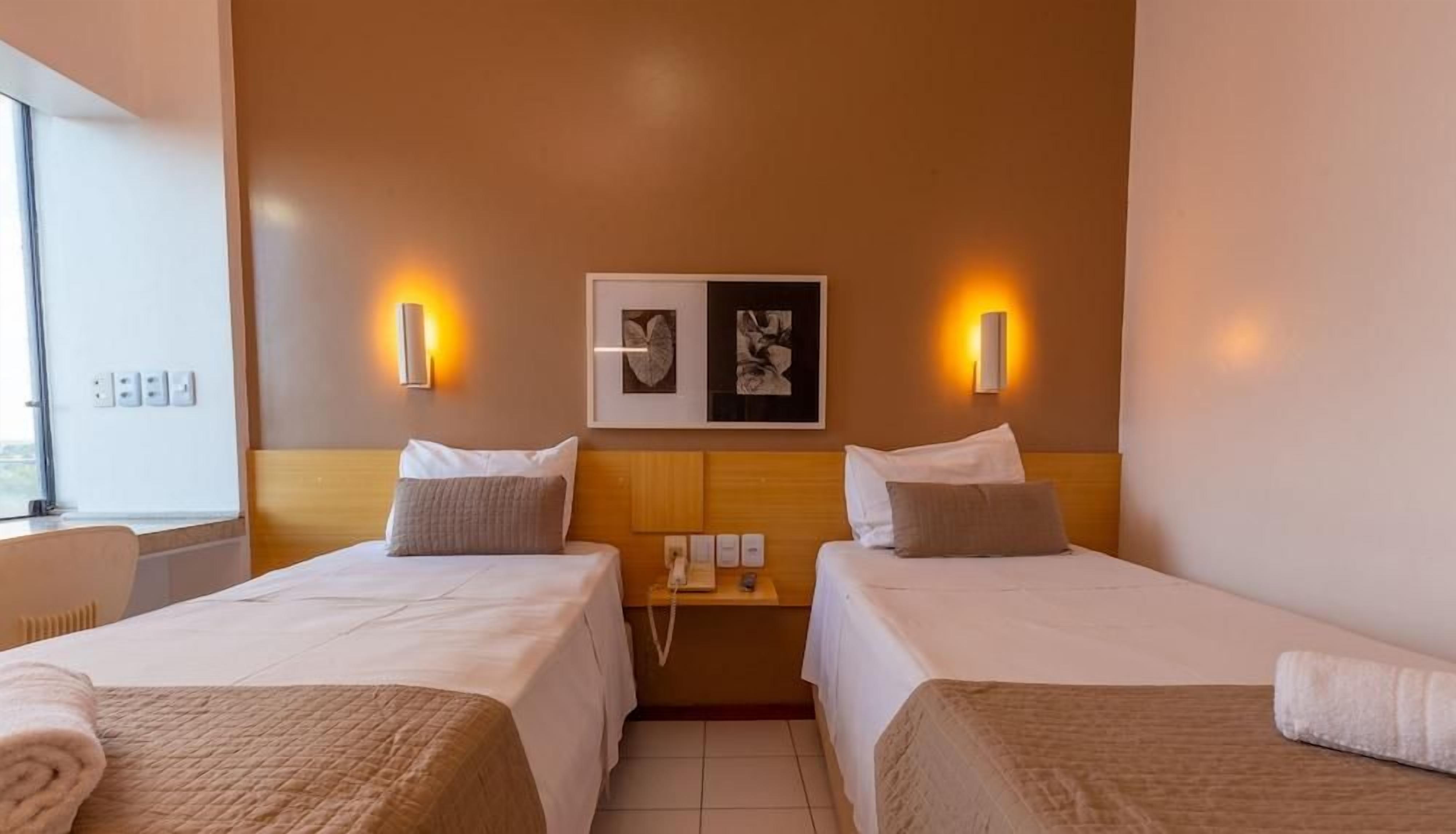 A hotel room with two beds, a bedside table, a wall-mounted phone, and artwork.