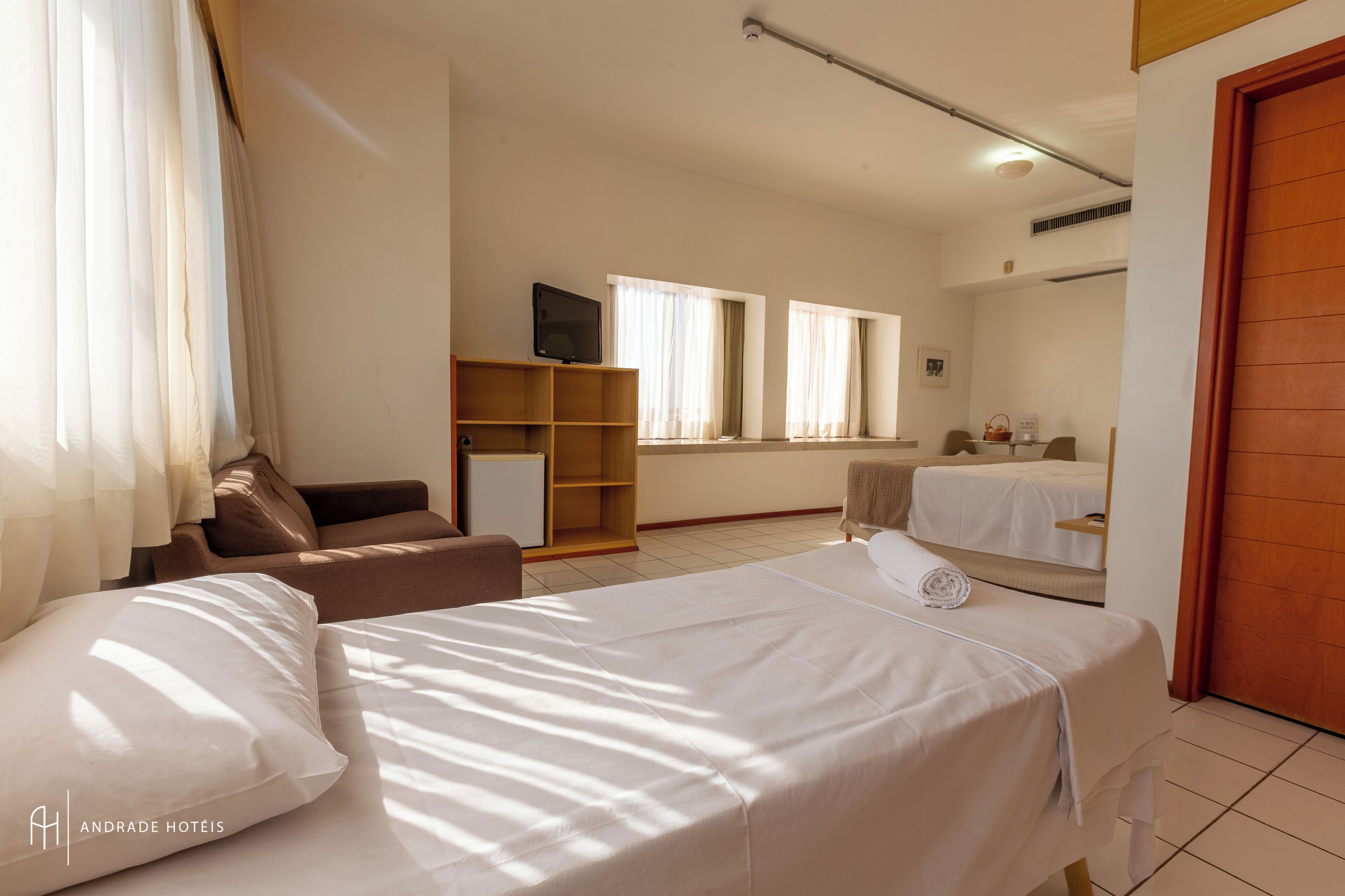 A hotel room with two beds, a TV, a desk, and a window with curtains.