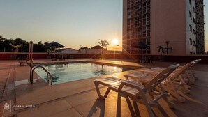 Zona de piscina de hotel con sillones de descanso y un edificio al fondo.
