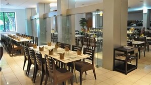 Un restaurante espacioso con varias mesas y sillas, pilares grandes y vistas al área de la cocina.