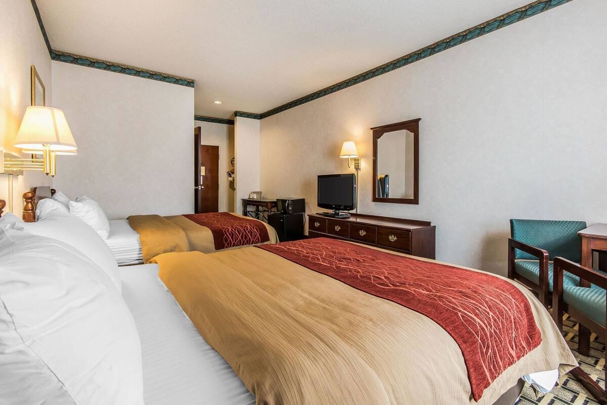 A hotel room with two beds, a desk, a television, and a mirror.