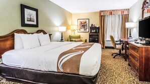 A hotel room with a large bed, a desk with a computer, a chair, a television, and a lamp. - Quality Inn Whiteville North (Whiteville)