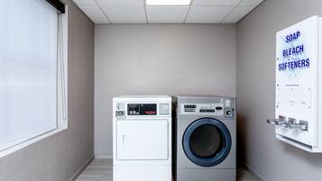 Een wasserette met twee wasmachines, een raam en een dispenser voor zeep en bleekmiddel, bevestigd aan de muur.