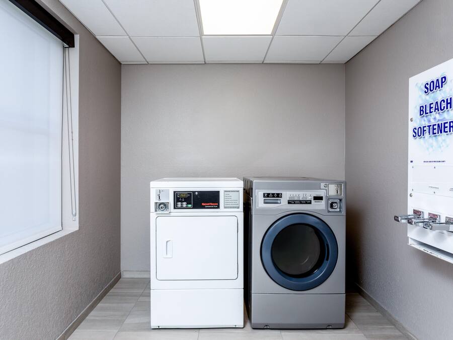 A laundry room with two washing machines, a window, and a wall-mounted soap and bleach dispenser.