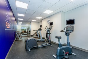 Un gimnasio con máquinas de cardio, un reloj de pared y texto motivacional.