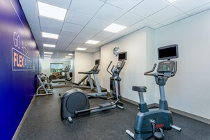 A gym with cardio machines, a wall clock, and motivational text.