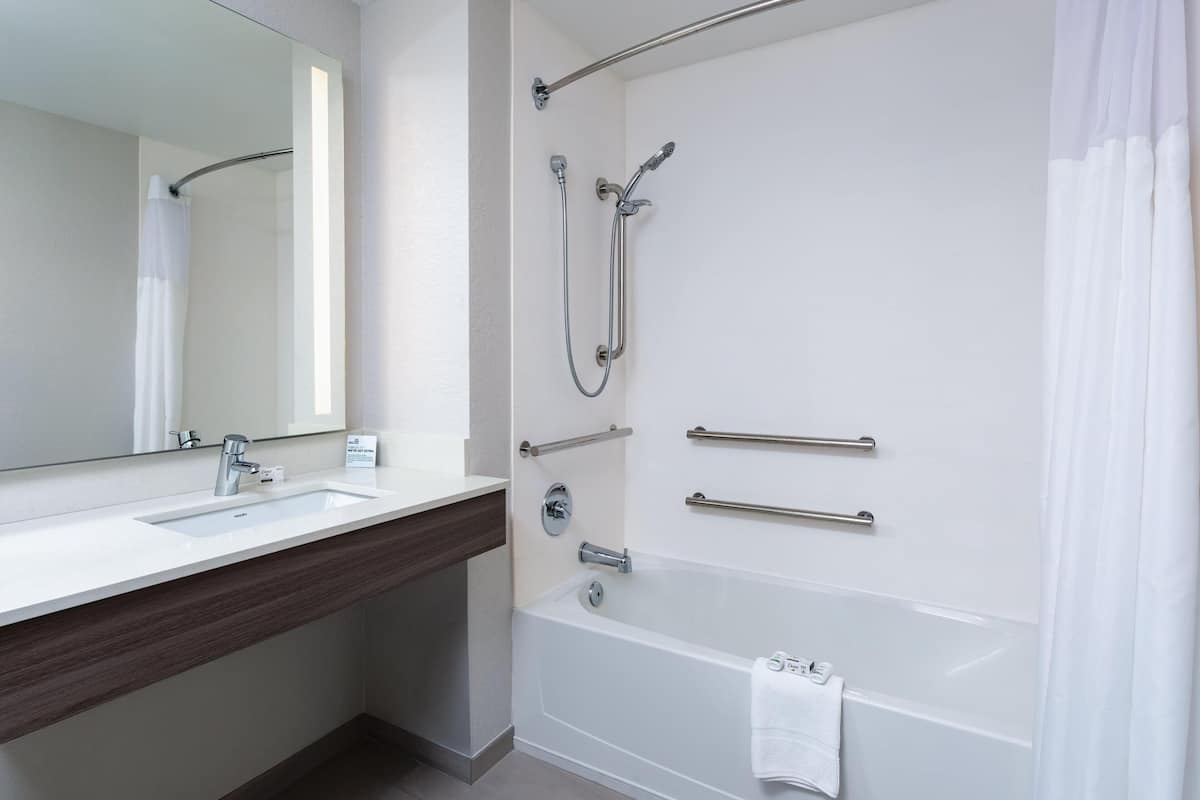 A modern bathroom with a white sink, mirror, and bathtub.