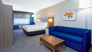 Una habitación de hotel con cama, sofá azul, mesa de centro de madera, lámpara de pared y un cuadro.