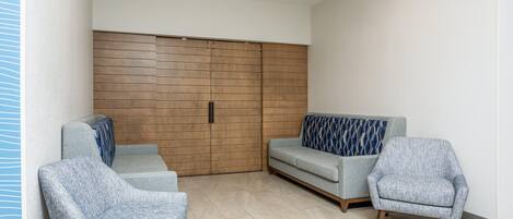Un salon moderne avec un canapé, deux fauteuils, un mur recouvert de panneaux en bois et une porte coulissante.