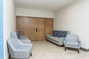 A modern living room with a sofa, two armchairs, a wooden panel wall, and a sliding door.