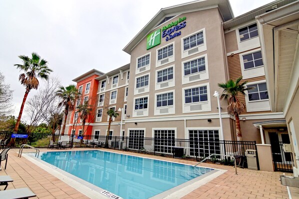 Edificio de Holiday Inn Express con piscina, palmeras y un patio amurallado.