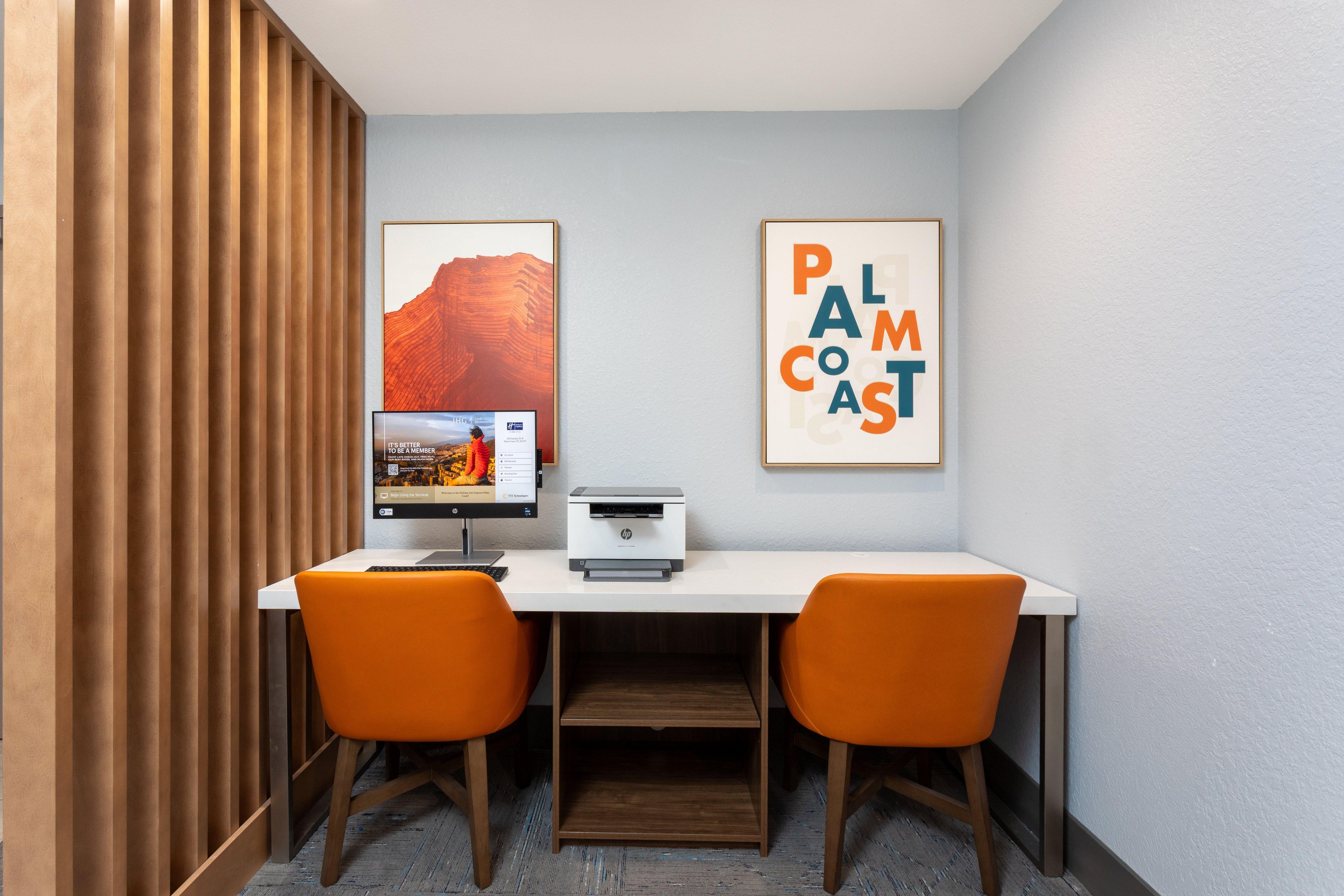 Un espace de travail comprenant un bureau, deux chaises, une imprimante et des tableaux encadrés accrochés au mur.