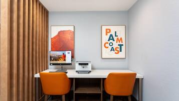 Een werkplek met een bureau, twee stoelen, een printer en ingelijste foto’s aan de muur.