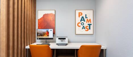 Un espace de travail comprenant un bureau, deux chaises, une imprimante et des tableaux encadrés accrochés au mur.