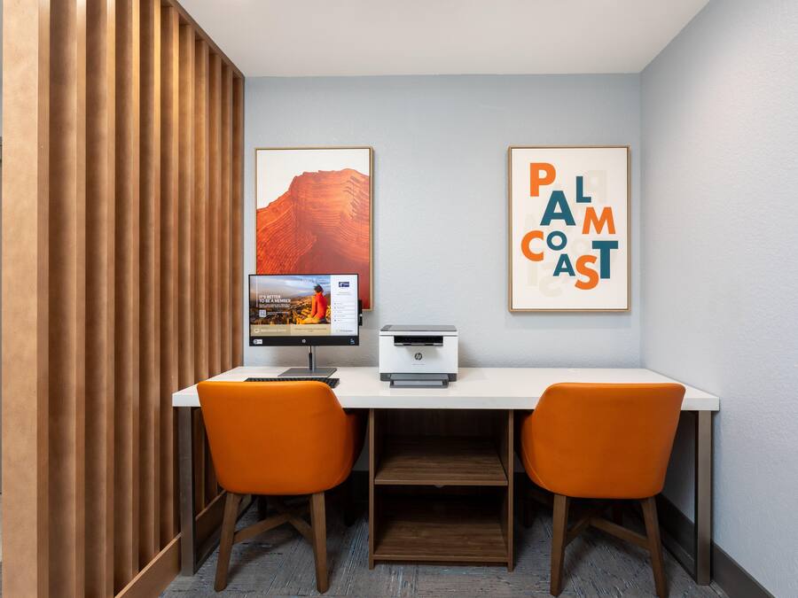 Un espacio de trabajo con un escritorio, dos sillas, una impresora y cuadros en la pared.