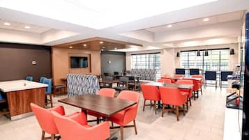 A modern dining area with multiple tables and chairs, a kitchen counter, and a large window providing natural light.