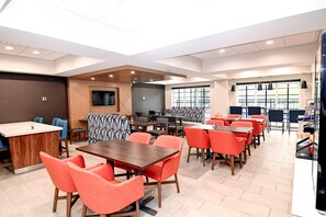 A modern dining area with multiple tables and chairs, a kitchen counter, and a large window providing natural light.