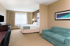 A hotel room with a bed, a desk, a chair, a sofa, a television, and a framed picture on the wall. - Holiday Inn Express & Suites Palm Coast - I-95 (Palm Coast)
