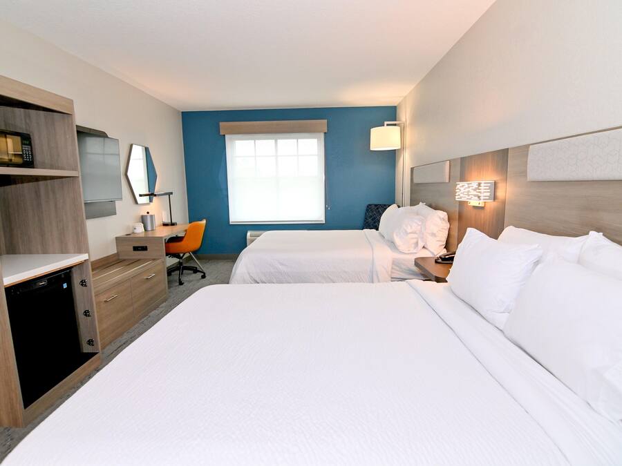 Ein Hotelzimmer mit zwei Betten, einem Schreibtisch, einem Stuhl, einer Mikrowelle und einem Fenster.
