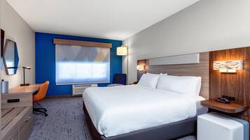 Une chambre d’hôtel avec un grand lit, un bureau, une chaise, une commode, une fenêtre et une lampe fixée au mur.