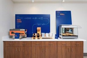 A breakfast station with a panini press, a box of fresh panini, and a display of breakfast items. - Holiday Inn Express & Suites Palm Coast - I-95 (Palm Coast)