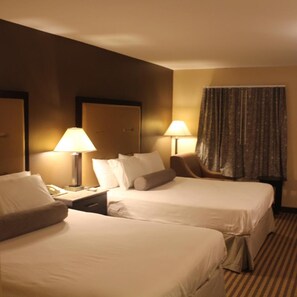 A hotel room with two beds, bedside tables, lamps, a chair, and a window with curtains. - Travelodge by Wyndham Bellmawr (Bellmawr)