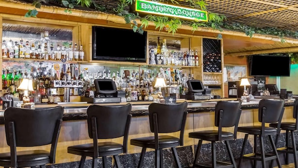 A bar area with a bamboo sign, multiple liquor bottles, bar stools, and a television screen. - Uptown Oasis San Jose Airport (San Jose)
