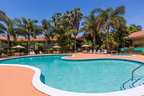 A swimming pool with lounge chairs and umbrellas, surrounded by palm trees and a building with a red-tiled roof. - Uptown Oasis San Jose Airport (San Jose)