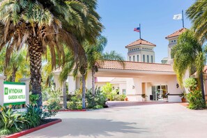 A hotel entrance with a sign, palm trees, and a building with a tiled roof. - Uptown Oasis San Jose Airport (San Jose)
