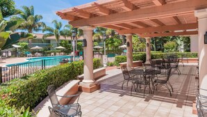 A covered outdoor area with tables and chairs, a pool, and palm trees. - Uptown Oasis San Jose Airport (San Jose)