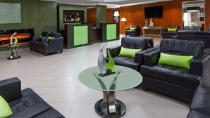 A hotel lobby with leather sofas, a glass table, a reception desk, and a fireplace. - Uptown Oasis San Jose Airport (San Jose)